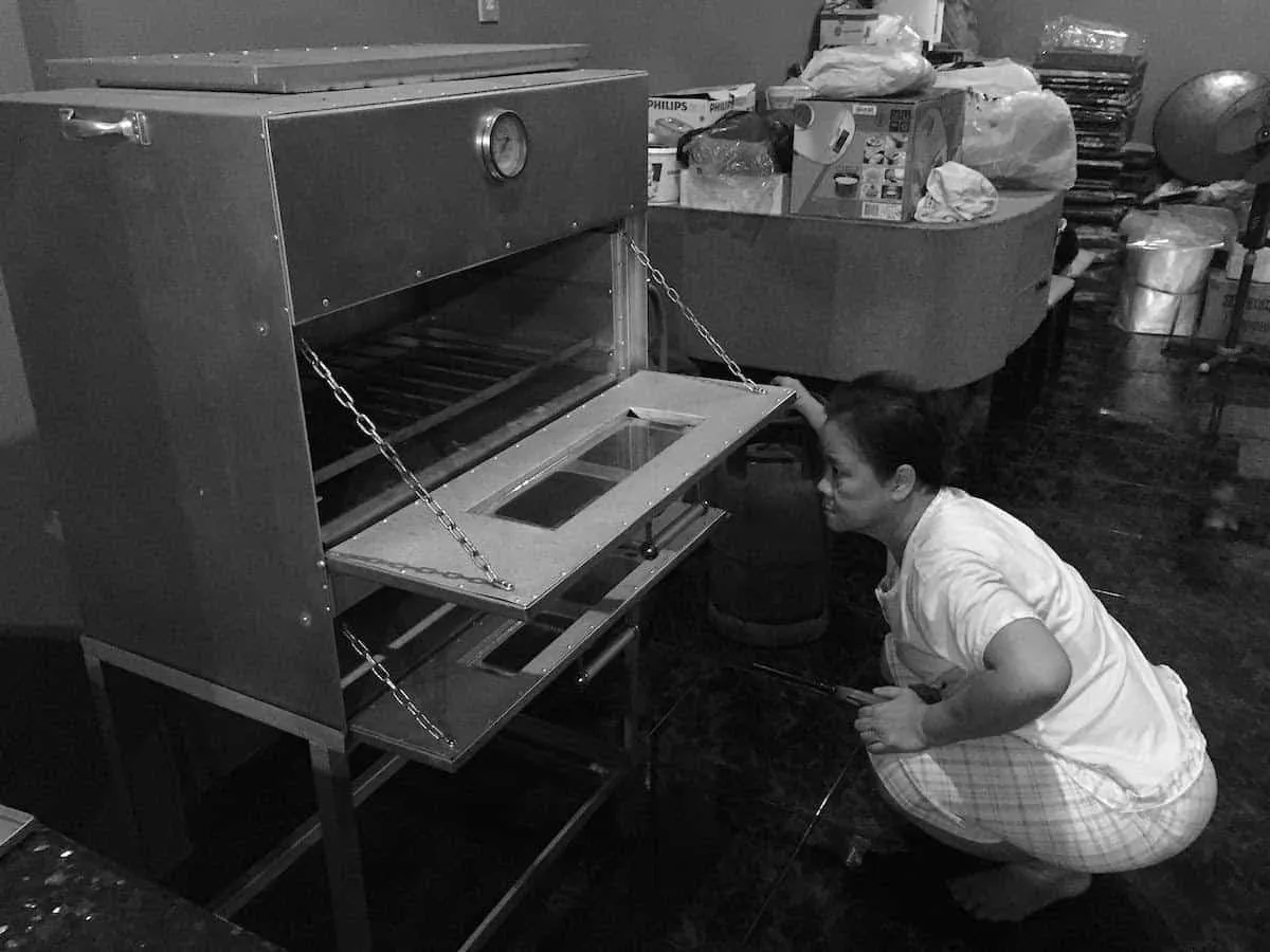 Ibu Tjang Dju Kui memeriksa oven di dapur rumah, waktu dulu